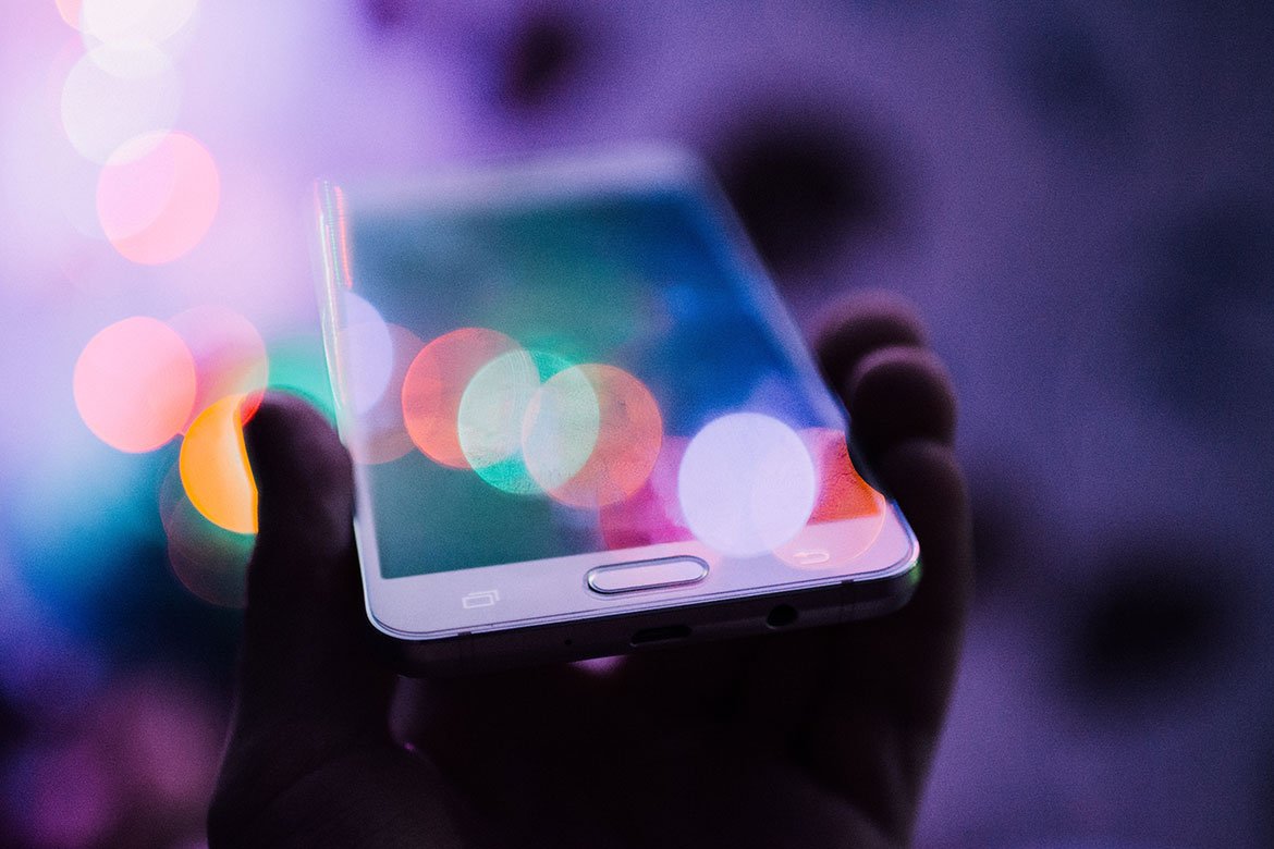 A person holding up a smartphone in their hand with colorful bokeh circles over its screen